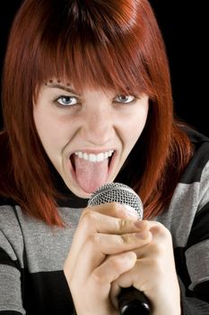 A happy redhead girl holding a karaoke microphone and screaming.

Studio shot.