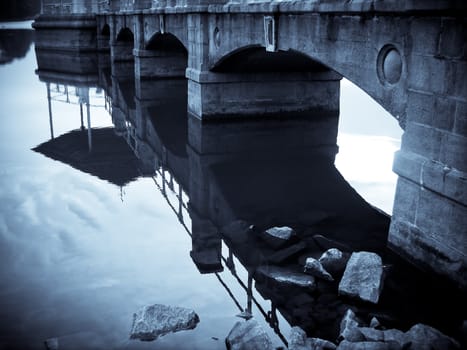Blue bridge on the water with rocks. The reflection of the bridge can be seen on the waters.