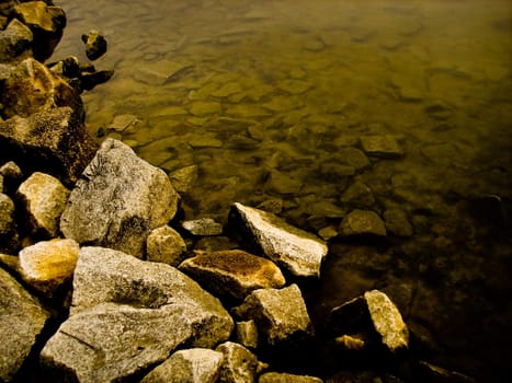 Yellow rocks along the waters, with smaller rocks submerged under the water.