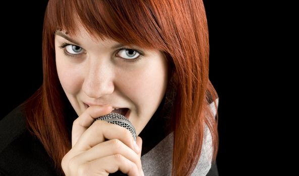 Happy redhead girl singing karaoke on a microphone.

Studio shot.