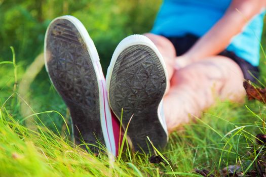 Pink sneakers on girl legs on grass during sunny summer day.