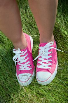 Pink sneakers on girl legs on grass during sunny summer day.