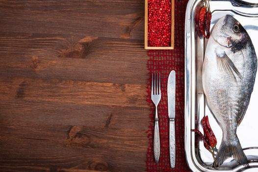 Dorado fish on a wooden surface with red pepper