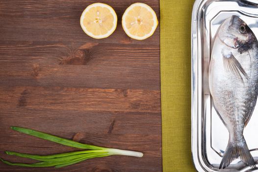 Dorado fish on a wooden surface with slices of lemon and a green onions