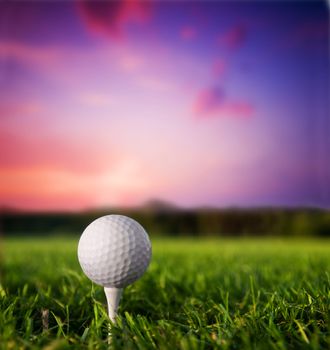 Golf ball on tee. Green grass, sunset.