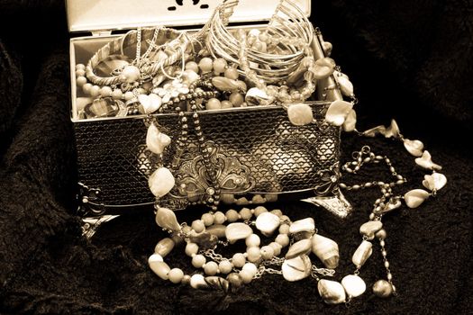 A black and white image of a silver box spilling jewellry on a black fur