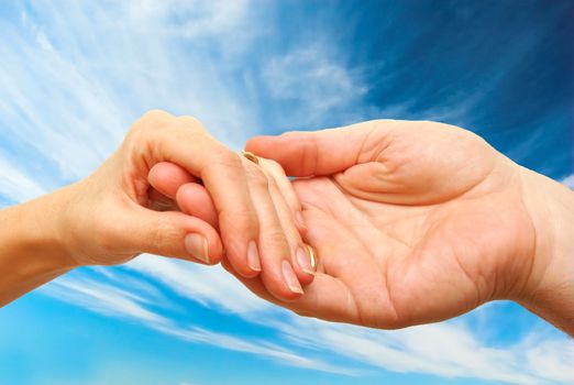 Two hands - woman and man touch each other in delicate, subtle way on sky background