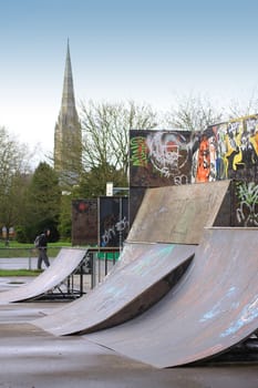 Graffiti covered curved steel skateboard ramps located in Salisbury wiltshire. A portrait format image with the spire of Salisbury cathedral visible in the background.