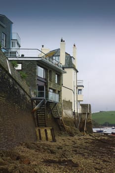 Low tide at Salcombe in devon. A portrait format image showing sea shore buildings with access to the shore via stairways.