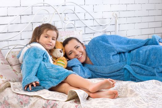 Mother and her five year old daughter are in robes on the bed
