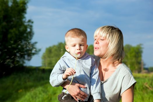 Kid and mother blowing dandelion. Spring time