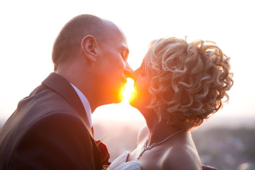 Happy bride and groom kissing outdoors at sunset