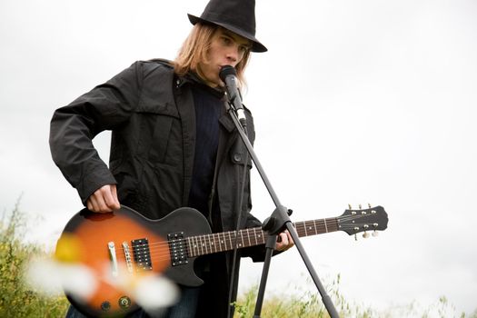 Man in hat playing guitar outdoors.