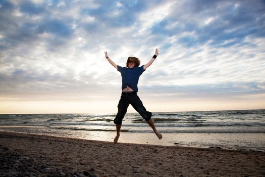 Happy young man jumping on the beach during sunset