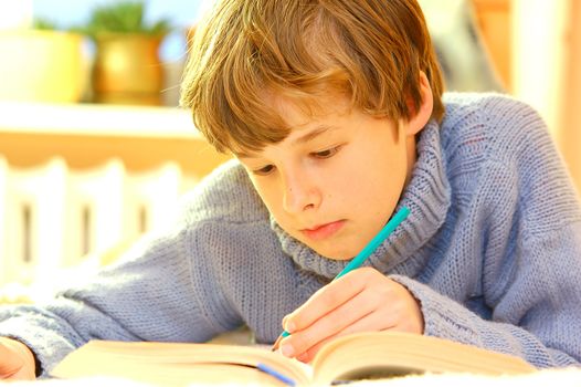 Boy doing homework on bed in sunny bedroom