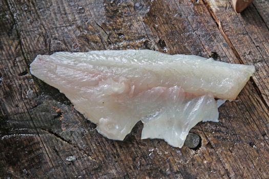 A fillet from a freshly cleaned Largemouth Bass sitting on an outdoor cleaning board.