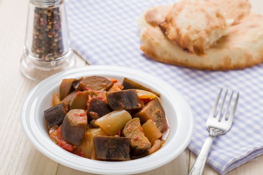 Cooked stewed eggplants in plate served with bread, fork on linen napkin and wooden table