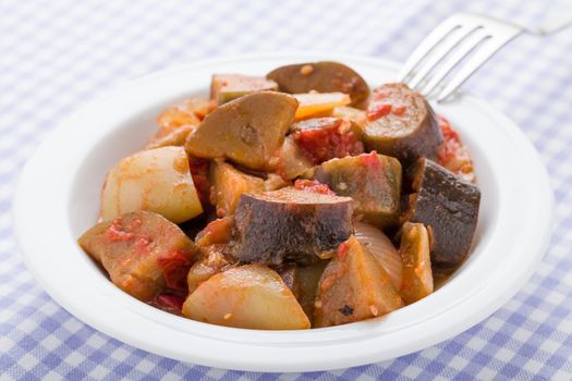 Cooked stewed eggplants in plate close-up with fork served on checkered linen napkin