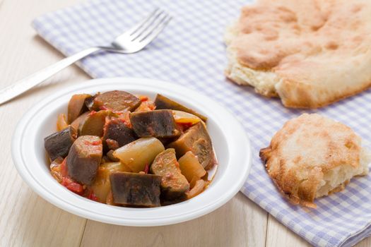 Cooked stewed eggplants in plate served with bread, fork on linen napkin and wooden table