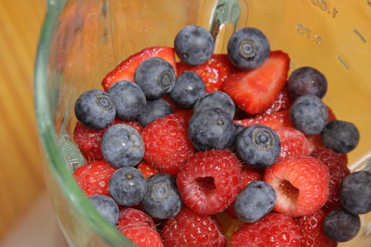 Fruit, including blueberries, raspberries, and strawberries, in a blender, about to made into a smoothie.
