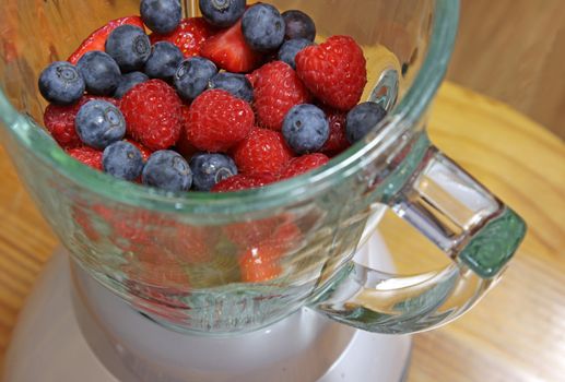 Fruit, including blueberries, raspberries, and strawberries, in a blender, about to made into a smoothie.
