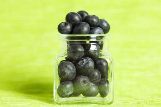 blueberries in a glass jar on a green background