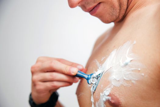 Young man shaving his chest, torso using a gel and a razor
