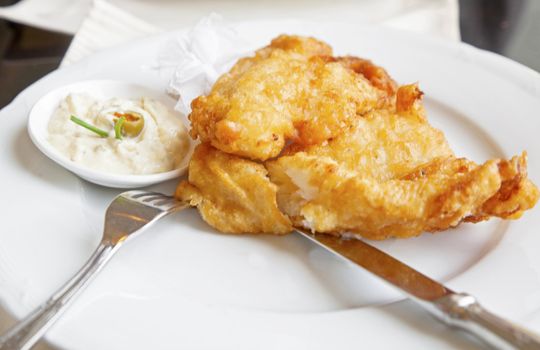 Plated up on white porcelain china battered fish plated with horseradish sauce decorated with chives and green olive. Shot location Bombay, india