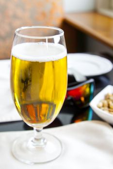 Vertical Interior corner detail of black top table with glass of beer, mirrored sunglasses by a window ledge in daylights