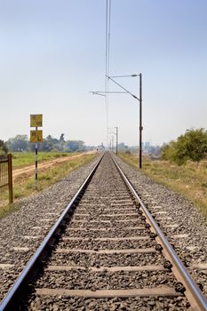 Vertical landscape of railroad tracks in Indian cutting across the rural countryside along the outskirts of o Gujarat village towards the city of Surat. Typical scene with litter thrown around and locals walking close by