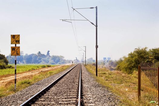 Horizontal landscape of railroad tracks in Indian cutting across the rural countryside along the outskirts of o Gujarat village towards the city of Surat. Typical scene with litter thrown around. Monotone