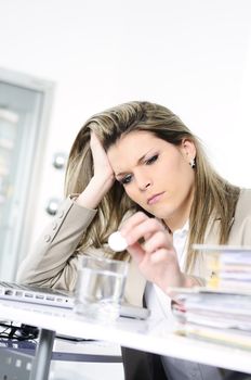 young woman stressed at work, taking an aspirin cahet