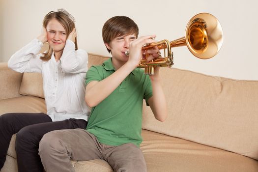 Photo of a brother playing his trumpet too loudly, or badly, and annoying his sister.