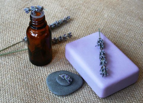 Lavender flowers, bottle of essential oil and soap on sackcloth background in a spa composition 