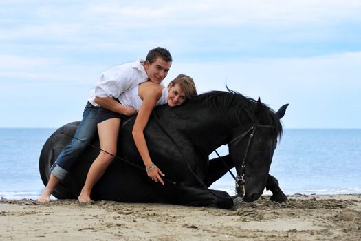 beautiful black stallion laid down on the beach with young couple