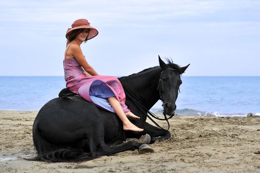 beautiful black horse laid down on the beach and young woman