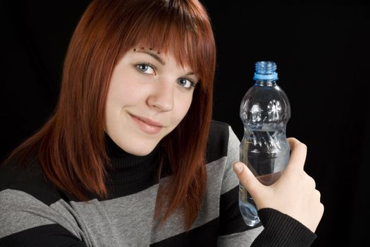 A beautiful redhead girl holding a bottle of water in her hand and looking at the camera.

Studio shot.