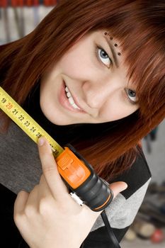 Beautiful redhead girl using measuring tape in workshop and pointing at 25cm to allude to the length of male reproductive organ, penis. Ironic.

Studio shot.