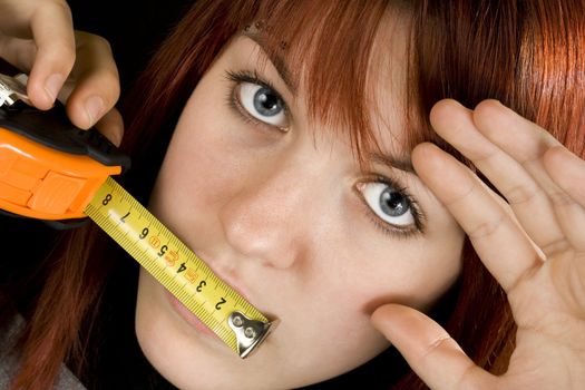 Beautiful redhead girl with blue eyes with a measuring ruler meter tape on her mouth.

Studio shot.