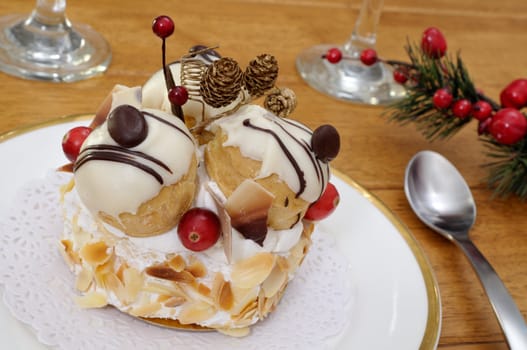 Choux pastry filled with cream and iced with vanilla and chocolate on a wooden table with Christmas decoration