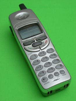A silver and dark gray cordless telephone rests on a green backdrop. The phone has a stubby antenna and is showing that there are messages waiting.
