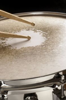 Drumsticks playing on a well-worn snare drum.