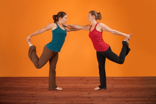 Two Caucasian women perform yogasana over orange background