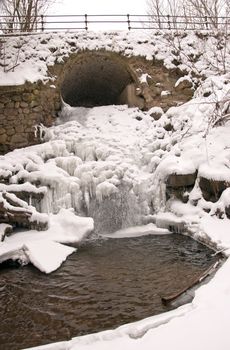 Stream water flow through arch waterfall ice icycles frozen in winter.