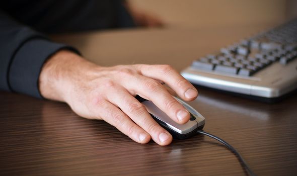 Hand of a man working at computer clicking on mouse on dark desktop