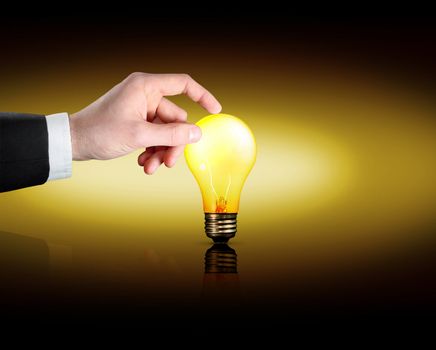 A business man's hand touches a lightbulb as it lights up.