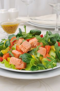 Vegetable salad with slices of salmon, roots, arugula, tomatoes and peppers, seasoned with mustard sauce with curry

