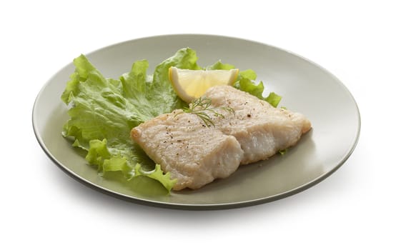 Fried fillet of pangasius with lettuce and lemon on the white plate