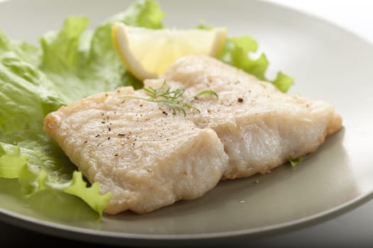 Fried fillet of pangasius with lettuce and lemon on the green plate