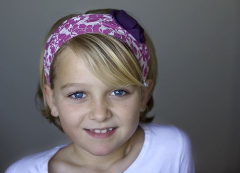 A young girl is smiling towards the camera, wearing a white and pink hairband. Positive feeling